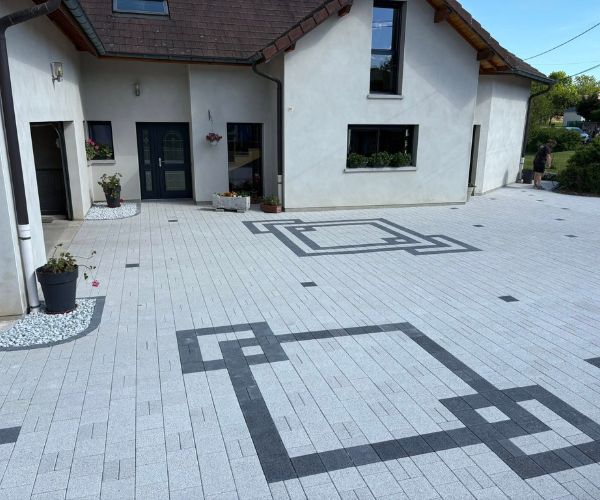 Entrée de maison aménagée en pavés Birkenmeier à Trepot avec massif décoratif en graviers blancs.