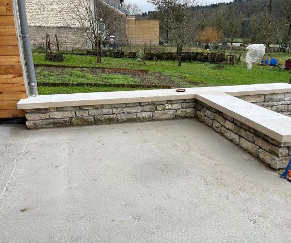 Mur en pierre avec chaperon en béton autour d’une terrasse à Quingey.